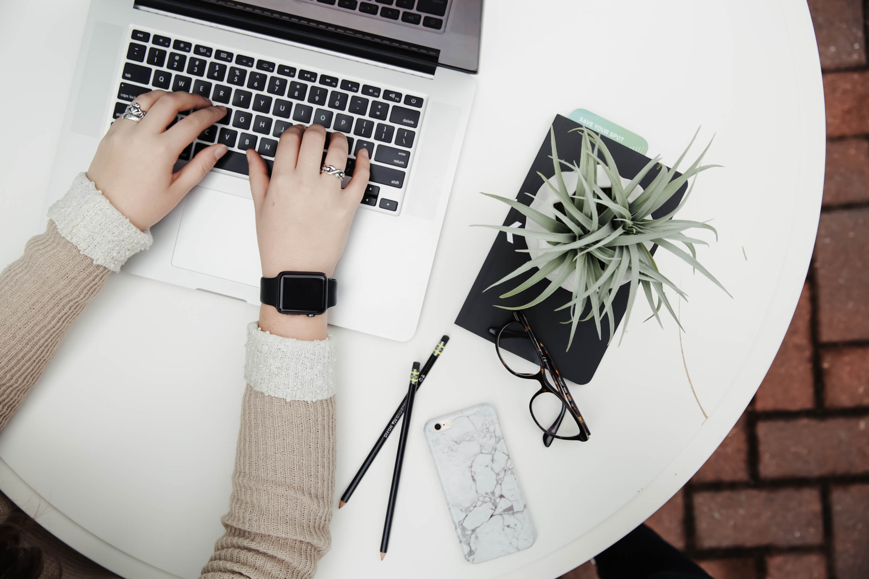 Hands typing on computer next to notepad and potted plant